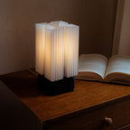 Novelty lamp with ribbed design on a wooden surface next to an open book