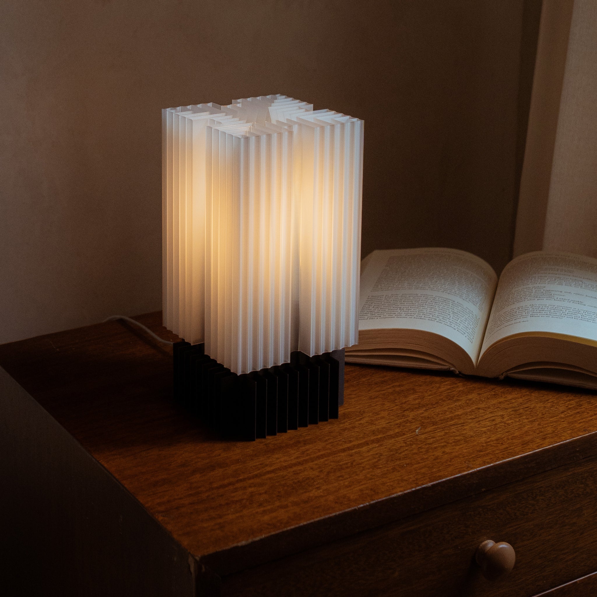 Novelty lamp with ribbed design on a wooden surface next to an open book