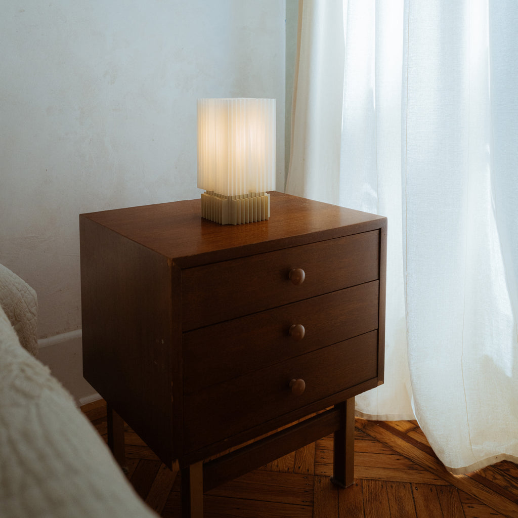 Wooden nightstand with a lamp next to a bed in a softly lit room.