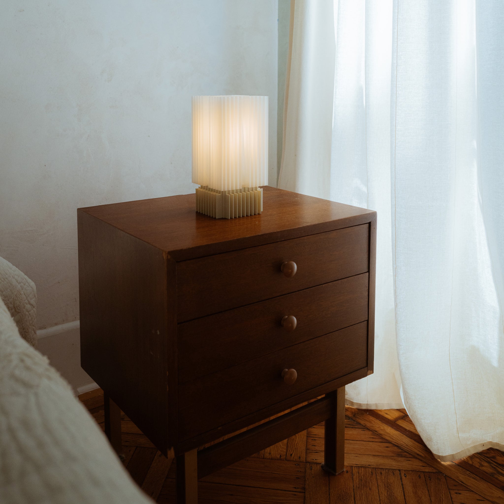 Wooden nightstand with a lamp next to a bed in a softly lit room.