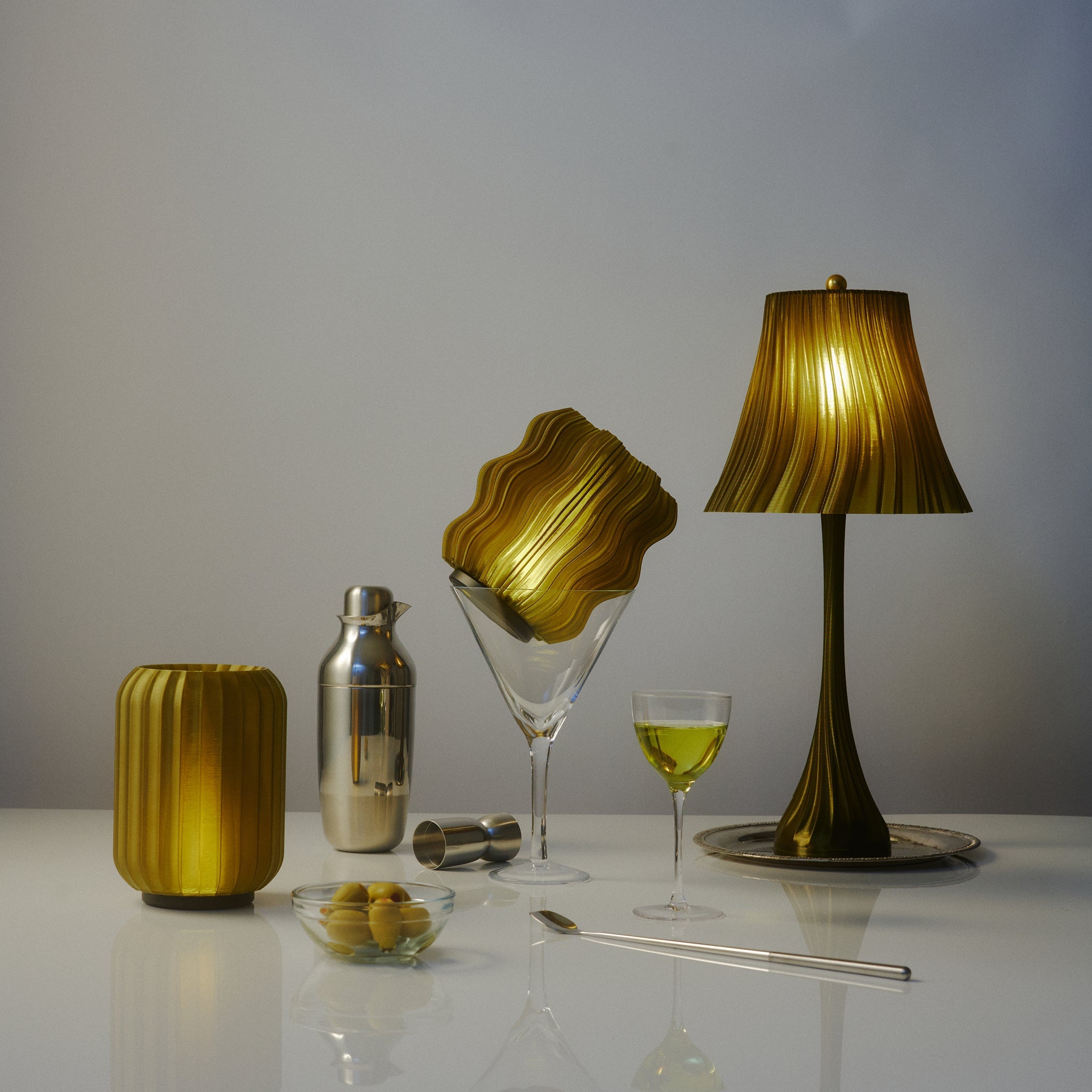 Decorative items including a lamp, vase, and glassware on a reflective surface with a neutral background.