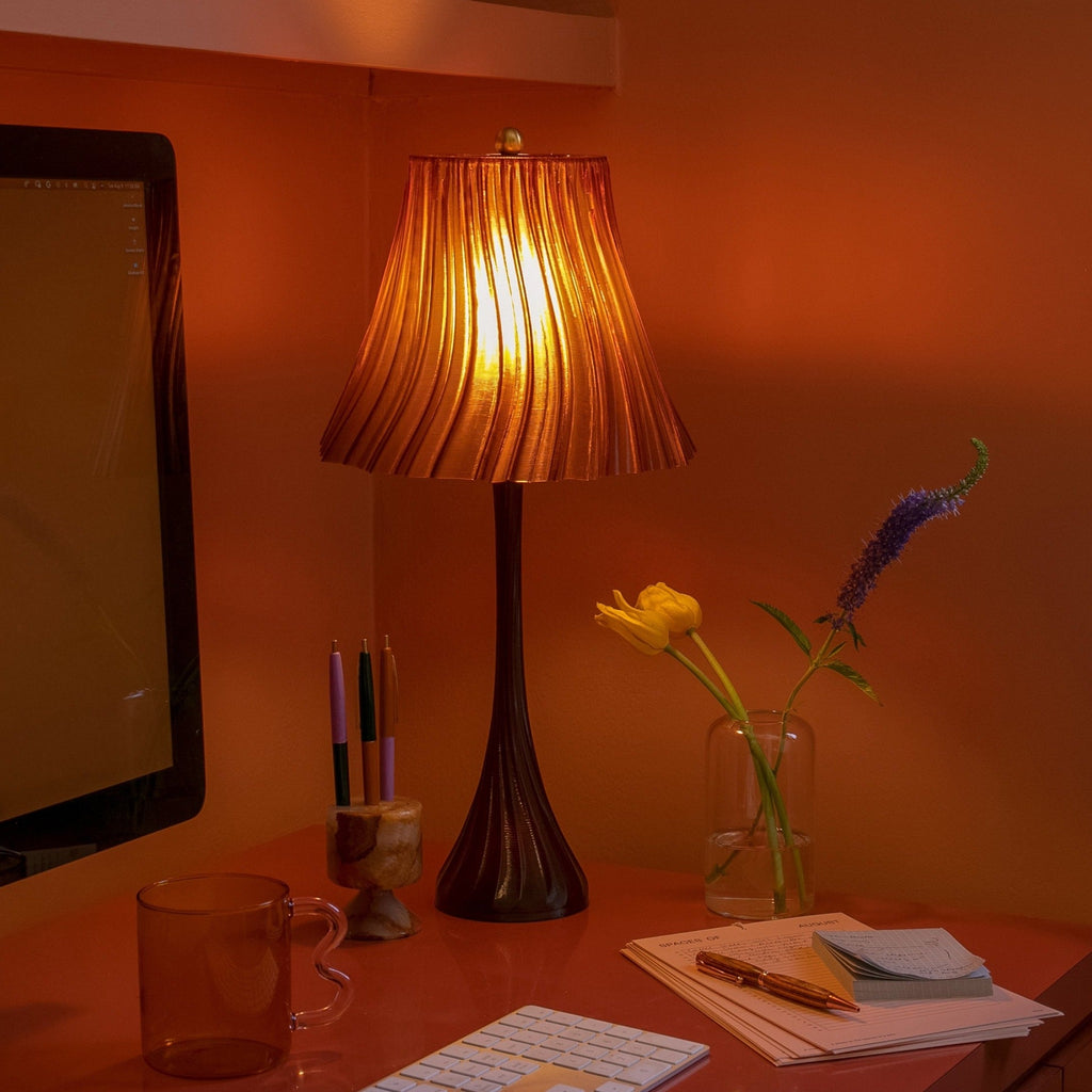 Orange room with a lamp, mug, flowers, and stationery on a desk.