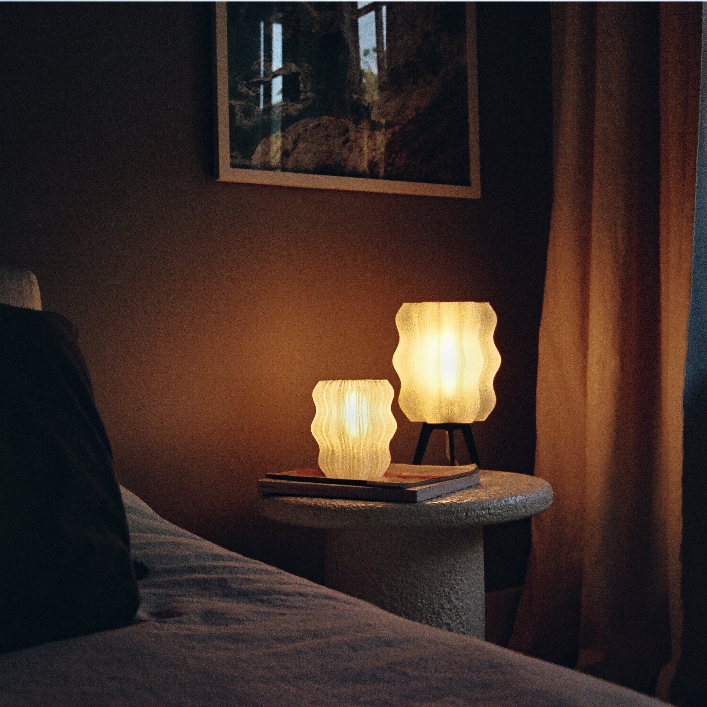 Two lit lamps on a bedside table in a dimly lit room.