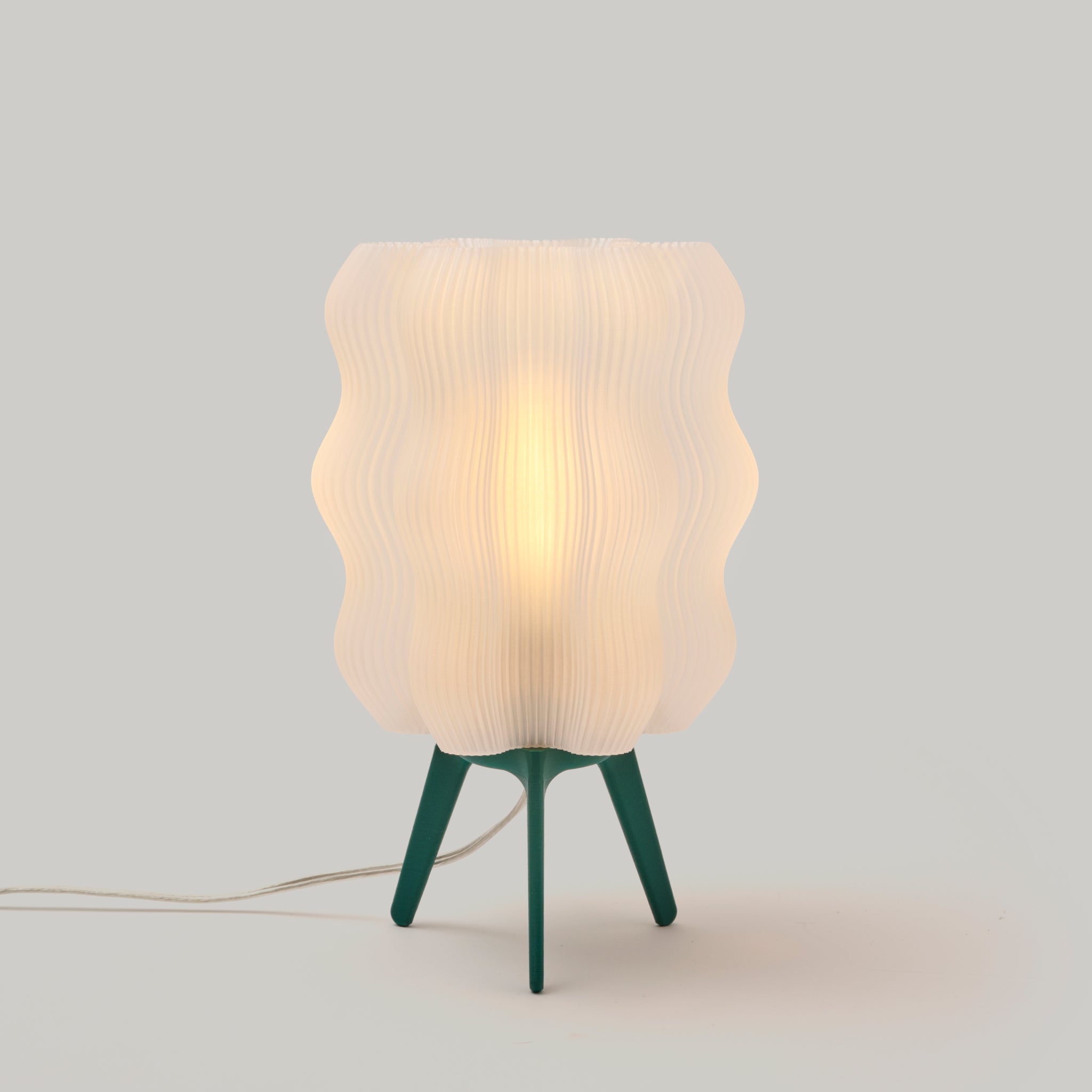 Table lamp with a ribbed white shade and green base on a light gray background