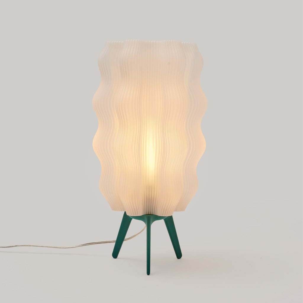 Table lamp with wavy beige shade and green base on a light gray background