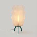 Table lamp with wavy beige shade and green base on a light gray background