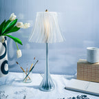 Decorative table lamp with a white shade on a surface with a vase, notebook, and other items.